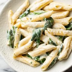 pasta with spinach and cream sauce in a white bowl on a marble countertop