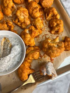 a tray filled with fried food next to a bowl of ranch dressing and a fork