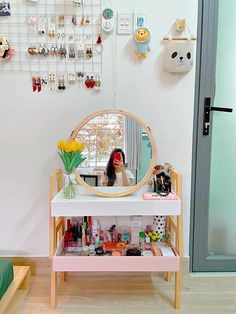 a woman standing in front of a mirror next to a shelf with various items on it