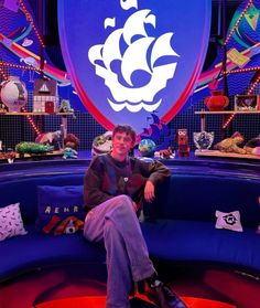 a man sitting on top of a blue couch in front of a large purple sign