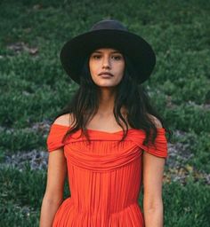 a woman in an orange dress and black hat poses for the camera with her hands on her hips