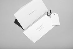 two white business cards sitting on top of each other next to a pair of glasses