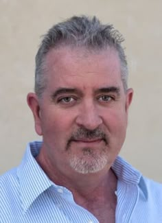 a man with grey hair and beard wearing a blue striped shirt looking at the camera