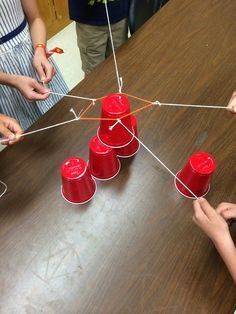 some red cups are on a table and one is connected to the other with string