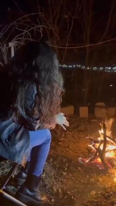 a woman sitting in front of a campfire at night