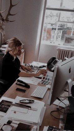 a woman sitting at a desk in front of a computer with papers on the table