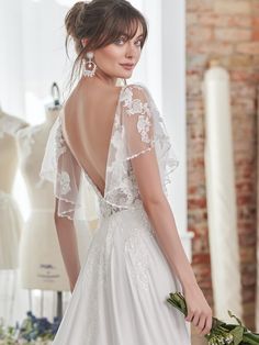 a woman in a white wedding dress holding flowers and looking at the back of her gown