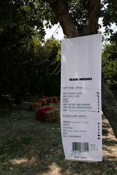 a bar menu hanging from a tree in the grass with hay bales behind it