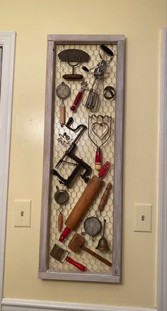 there are many different tools in the shadow box on the wall behind it is a hammer, pliers, scissors and other household items