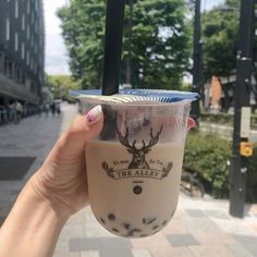 a person holding up a cup with milkshake on it in front of a building