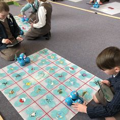 two boys playing with toys on the floor in a room full of other children sitting and standing around