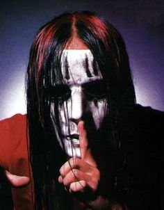 a man with long black hair and white makeup holding his finger up to the camera