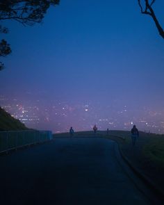 three people walking down a road at night with the city lights in the back ground