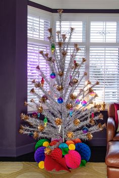 a brightly colored christmas tree in a living room with purple walls and leather chaires