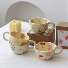 three flowered cups are sitting on a table next to a box and some candies