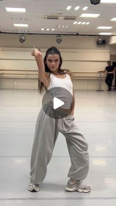 a woman in grey pants and white tank top doing a dance move with one hand