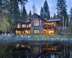 a large house sitting on top of a lake next to a forest filled with trees