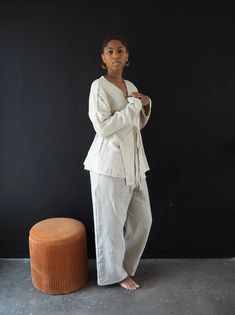 a woman standing in front of a black wall with her arms folded and looking off to the side