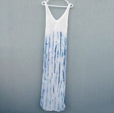 a white and blue tie - dye dress hanging on a clothes line against a gray wall