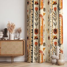 an orange and black patterned curtain hanging in front of a wooden cabinet with vases on it