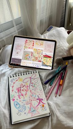 an open tablet computer sitting on top of a bed next to a drawing book and crayons