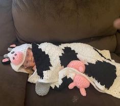 a baby wrapped up in a cow blanket on a couch next to a stuffed animal