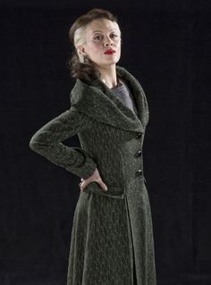 a woman in a green coat and black dress posing for the camera with her hands on her hips