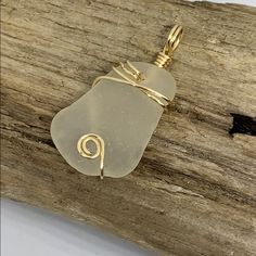 a yellow sea glass pendant sitting on top of a piece of drift wood with a wire wrapped around it