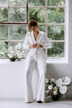 a woman standing in front of a window wearing a white suit