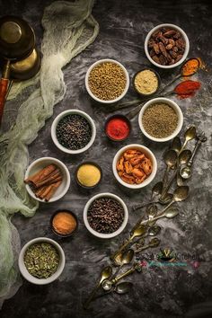 various spices and spoons are arranged in bowls on a gray surface with a green cloth