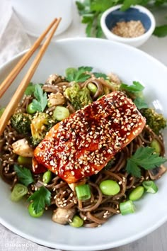 a white plate topped with meat and vegetables next to chopsticks on a table