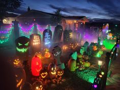 a yard filled with lots of pumpkins lit up in different colors and shapes at night