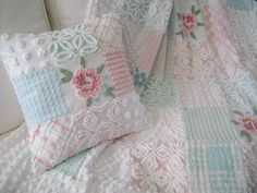 two decorative pillows sitting on top of a bed covered in white and pink quilts