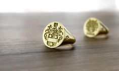 two gold rings sitting on top of a wooden table, one with a coat of arms