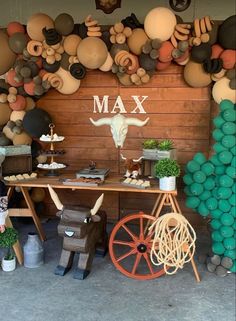 a table topped with lots of balloons next to a wall covered in fake animal heads