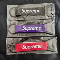 three supreme keychains in plastic packaging on a black surface with the words supreme printed on them