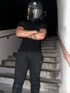 a man wearing a helmet and holding his arms crossed standing in front of some stairs