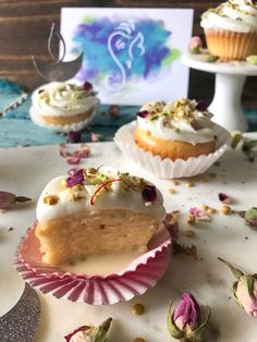 three cupcakes with white frosting and flowers on the table next to each other