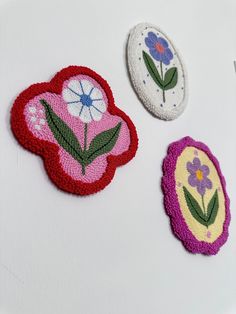 three embroidered patches with flowers on them sitting on a table next to scissors and thread