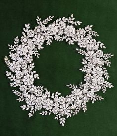 a wreath made with white flowers and leaves on a green velvet background for a wedding or special occasion