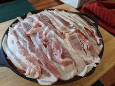 bacon cooking in a cast iron skillet on top of a wooden table next to a red towel