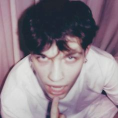 a young man is posing for the camera with his finger on his lips and wearing a white shirt