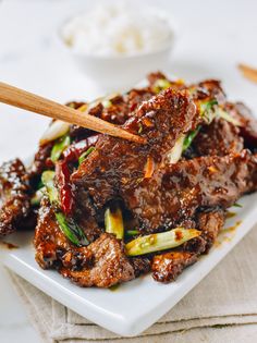 a white plate topped with meat covered in sauce and vegetables next to chopsticks