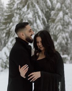 a man and woman standing next to each other in front of snow covered pine trees