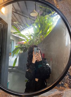 a woman taking a selfie in front of a round mirror with plants behind her