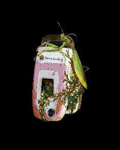 a green insect sitting on top of a pink and white box filled with plants in it