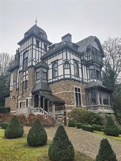 a large house with many windows and lots of bushes in front of it on a cloudy day