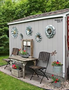 a small shed with flowers on the wall and some chairs around it in front of a table