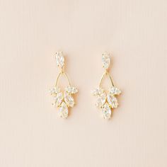 two pairs of gold and crystal earrings on a beige background, with the top one in white