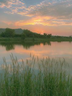 the sun is setting over a lake with tall grass